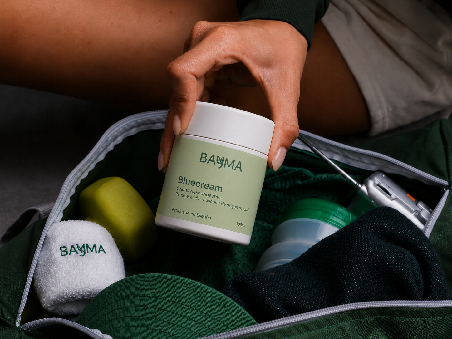 Envase de crema BAYMA con etiqueta verde presentado dentro de una bolsa de equipamiento deportivo